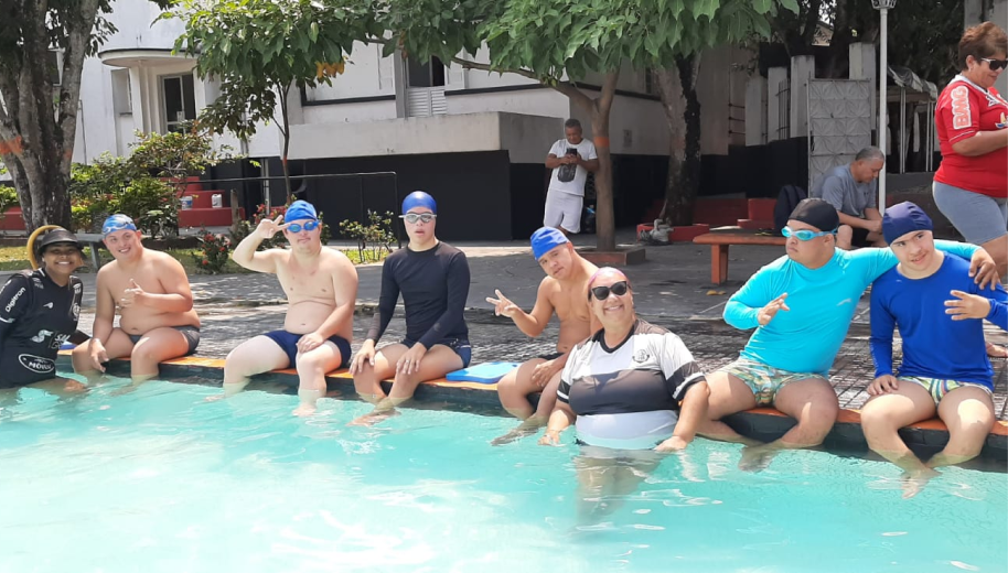 Grupo de Natação com seis rapazes com síndrome de Down sentados na piscina